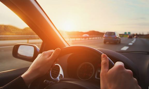 A person is driving a car on a highway during sunset.