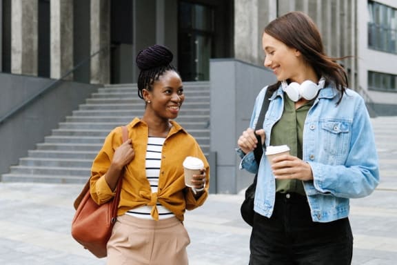 two women walking down the street talking and drinking coffee