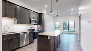 a kitchen with dark brown cabinets and a stainless steel dishwasher and microwave in front of a living room