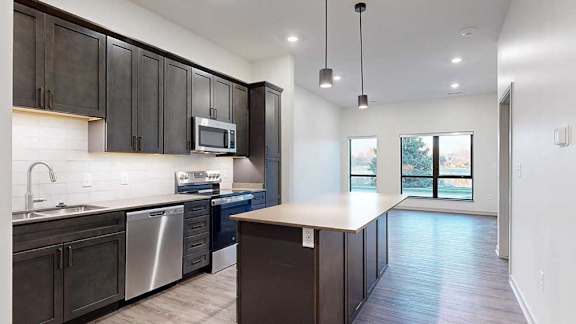 a kitchen with dark brown cabinets and a stainless steel dishwasher and microwave in front of a living room