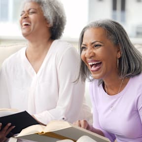 A group of people laughing and reading a book together.at The Orion Senior Apartments - Orange, CA, Orange