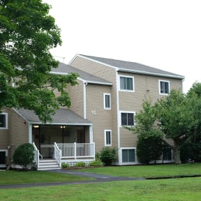 a large apartment complex with a grassy area and trees in front of it