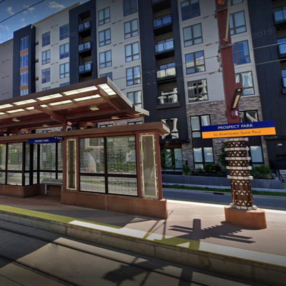 a rendering of a train station with a train on the tracks and a building in the background