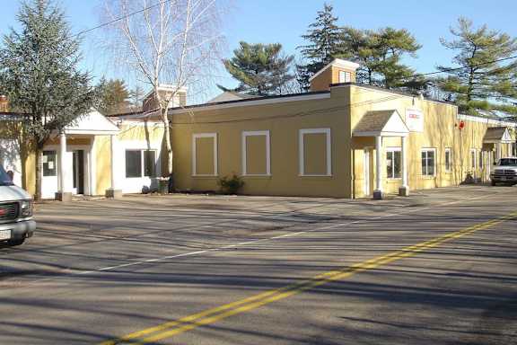 A yellow building with a white sign on it is in the middle of a parking lot.