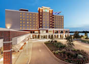 Thumbnail 3 of 7 - A hotel with a large front entrance and a landscaped area in front.