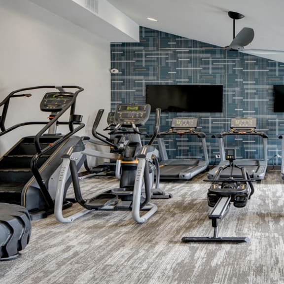 a gym with treadmills and televisions on the wall