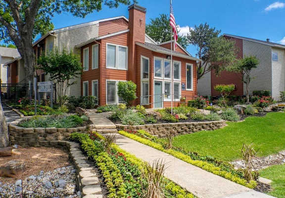 A house with a flag on the front porch is surrounded by a garden. at Infinity on the Oaks Apartments, Dallas, TX