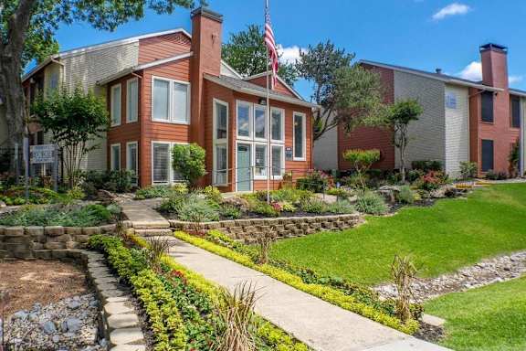 A house with a flag on the front porch is surrounded by a garden. at Infinity on the Oaks Apartments, Dallas, TX