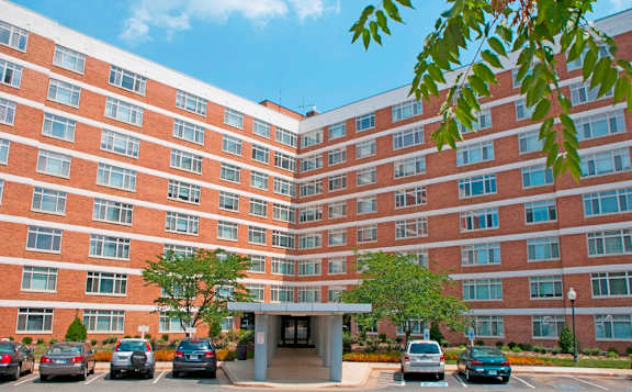 A large red brick building with a parking lot in front at Dominion Towers Apartments, Virginia