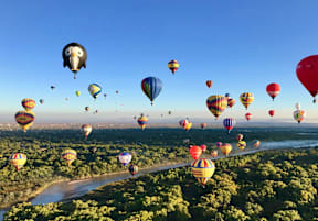 A group of colorful hot air balloons flying over a lush green landscape.
