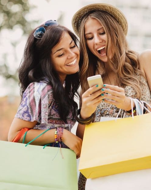 two women with shopping bags looking at a cell phone