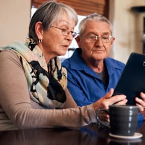 An elderly couple is sitting at a table with a tablet.at The Orion Senior Apartments - Orange, CA, Orange, 92866 at The Orion Senior Apartments - Orange, CA Apartments, Orange, California