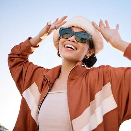 a woman wearing sunglasses and a hat with her hands in the air