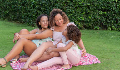 a mother and her two daughters sitting on a blanket on the grass