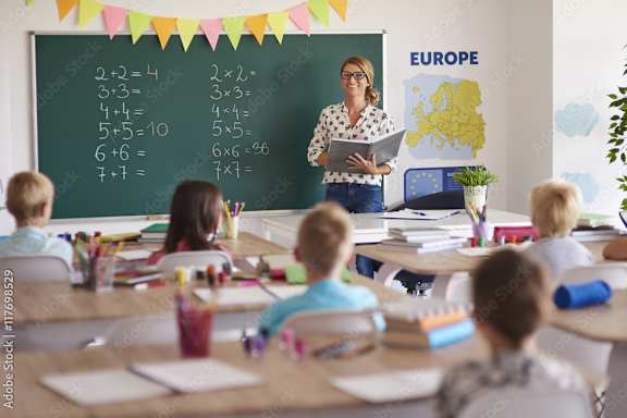 A teacher is teaching a class of children basic math equations on a chalkboard.