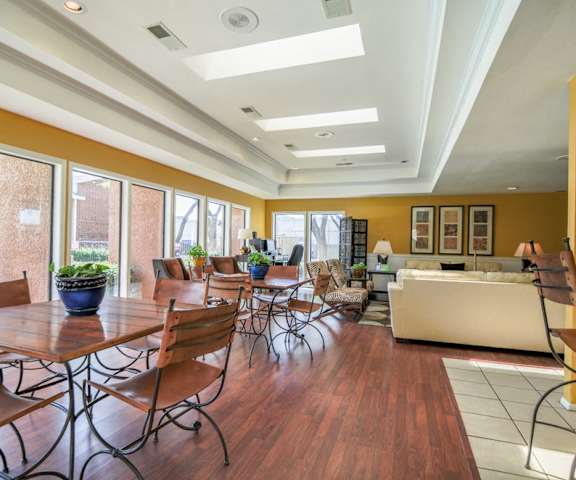 The resident lounge with couches, plush chairs, house plants, lamps, floor to ceiling windows showing the poor area, and coffee tables at Wildflower Apartment Homes. 