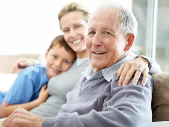 A family of three is sitting closely together on a couch.