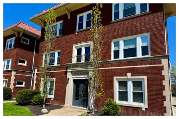 A red brick building with a black door and a balcony above it.