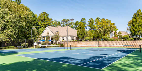 A tennis court surrounded by trees and a building in the background.