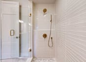 Thumbnail 13 of 13 - A white tiled bathroom with a gold shower head and faucet.