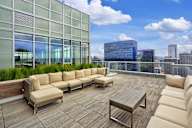 A wooden deck with a couch and a table in front of a glass building.