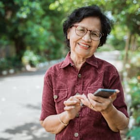 An elderly woman is smiling while looking at her phone.at The Orion Senior Apartments - Orange, CA, Orange, CA 92866