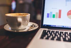 A laptop with a bar graph on the screen is placed on a table with a cup of coffee.