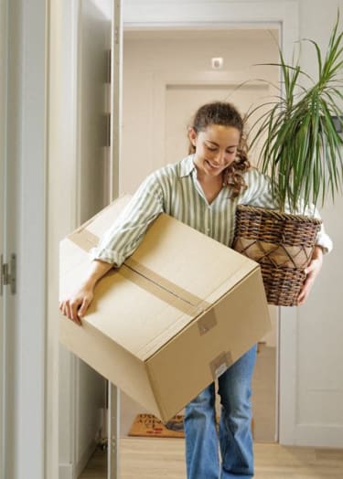 a woman carrying a box and a plant in a hallway