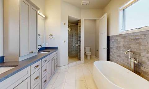 A bathroom suite featuring a freestanding soaking tub with brushed nickel fixtures, partitioned walk-in shower with surrounding full-height tile, and a private lavatory, all set atop marble-style flooring.