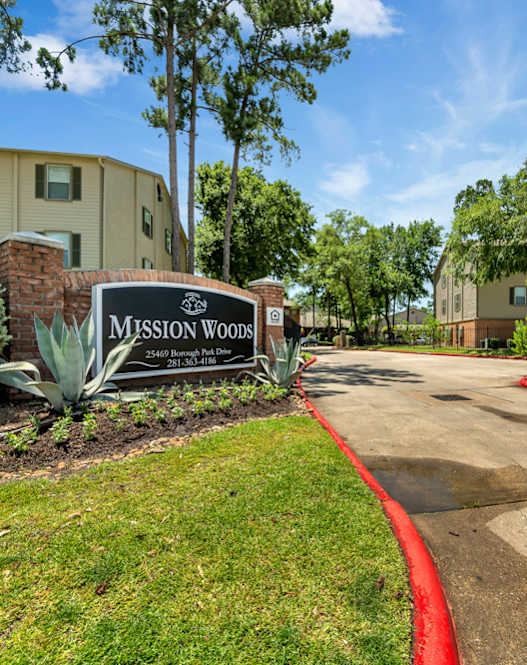 The image shows the entrance to Mission Woods Community with a sign and a flag.
