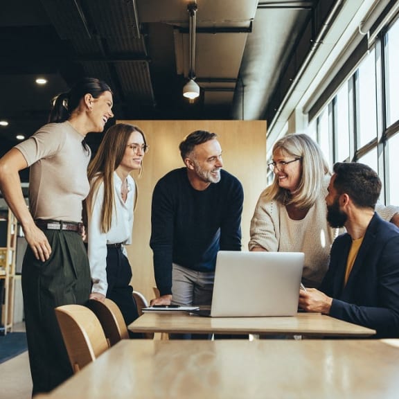 a group of people standing around a table looking at a laptop computer