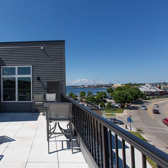 A balcony with a table and chairs overlooks a street and a mountain.