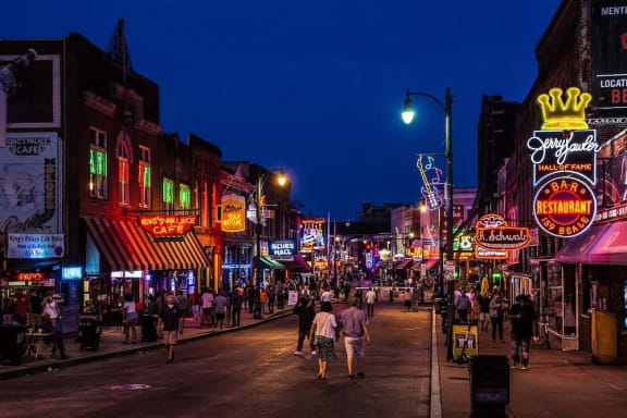 people walking down Beale Street in Memphis, TN at night with many neon signs lit up