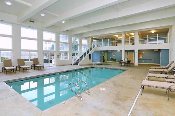 A large indoor swimming pool with lounge chairs and a staircase  at Vintage at Everett Senior Community, Everett, WA, 98201.