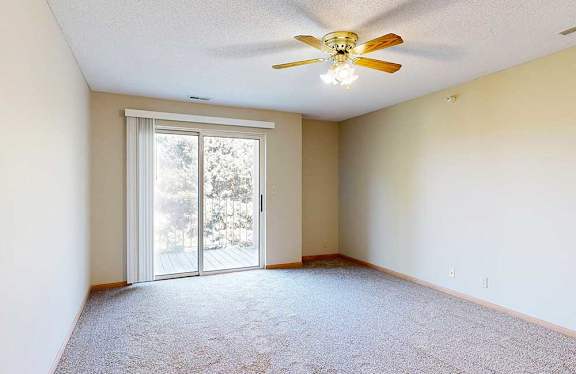 Spacious living room with sliding glass door to balcony, neutral walls, and ceiling fan with light.  Title: 1-Bed Horizon (#112)