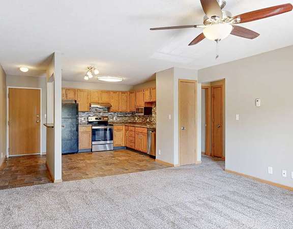 a carpeted living room with ceiling fan and open view into the kitchen