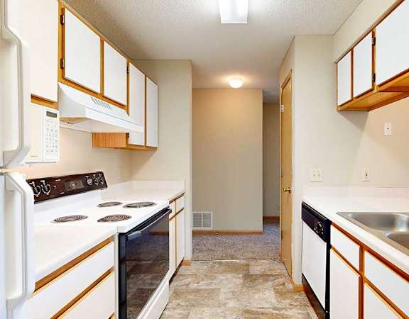 Galley kitchen with white appliances, electric stove, range hood, and wood-trim cabinetry.