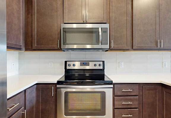 A close up on a stainless steel range and microwave in a kitchen with dark wooden cabinets.