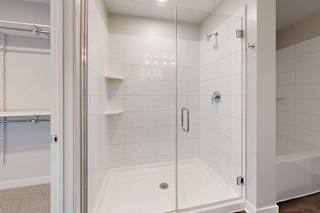 A white tiled shower with a glass door and a white tub next to it