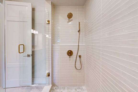A white tiled bathroom with a gold shower head and faucet.