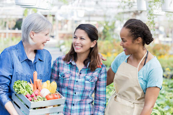 Three people holding a box of vegetables.
