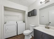 Thumbnail 12 of 15 - A small bathroom with a toilet, sink, and a washer and dryer.