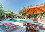 Thumbnail 5 of 27 - Pool deck with orange umbrella and lounge seating at The Colony Apartments, Universal City, TX 78148