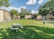 Thumbnail 25 of 27 - Fenced dog park with play equipment and picnic table at The Colony Apartments, Universal City, TX