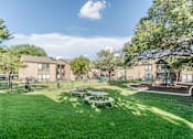 Thumbnail 26 of 27 - Courtyard with playground and picnic area surrounded by resident buildings at The Colony Apartments, Universal City, Texas