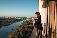 A woman is standing on a balcony with a camera, looking out at a cityscape.