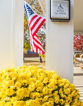 A sign on a pole that says "push to open" is next to a yellow flower bed.