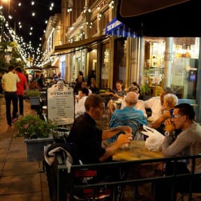 people sitting at tables outside of a restaurant at night