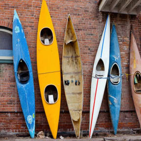 different colored kayaks against a brick wall
