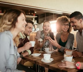 a group of people sitting around a table laughing and looking at a cell phone